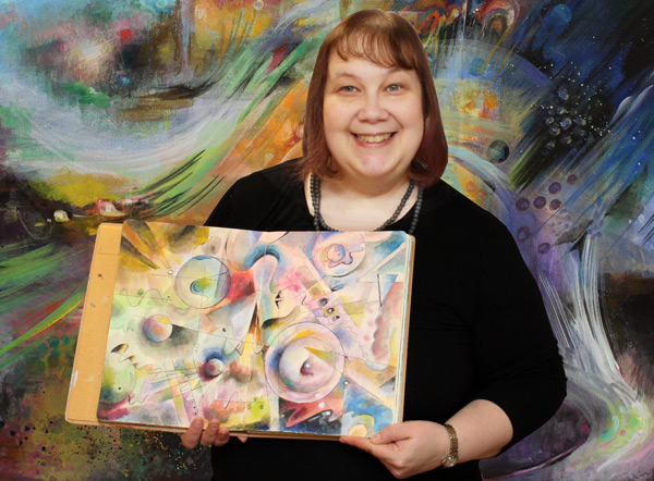 Paivi from Peony and Parakeet with an art journal and a canvas painting.