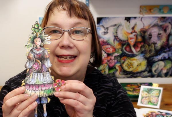 Paivi Eerola with one of her paper dolls showing the collage art pieces that she makes.