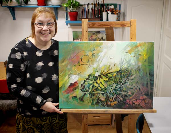 Artist Paivi Eerola holding her abstract painting Call of the Sun.